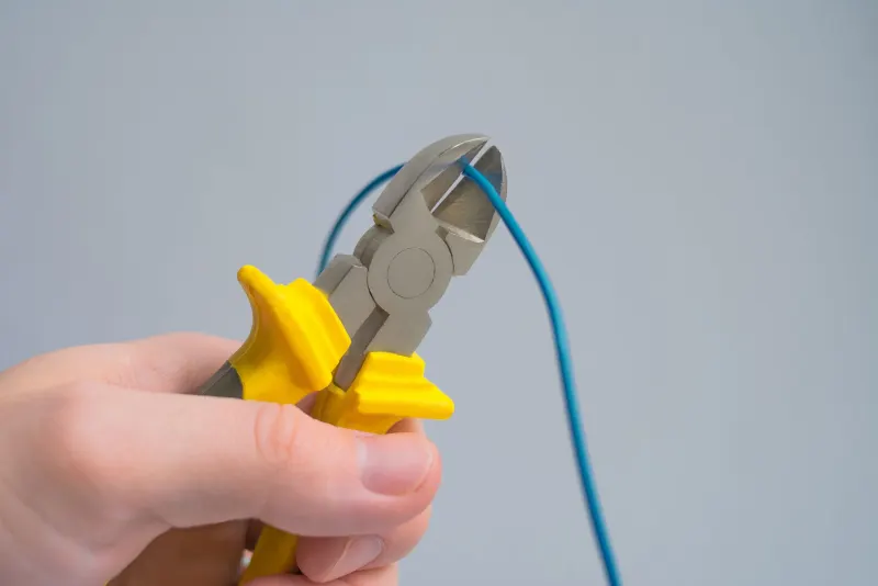 Hands cutting a blue electrical cable with pliers