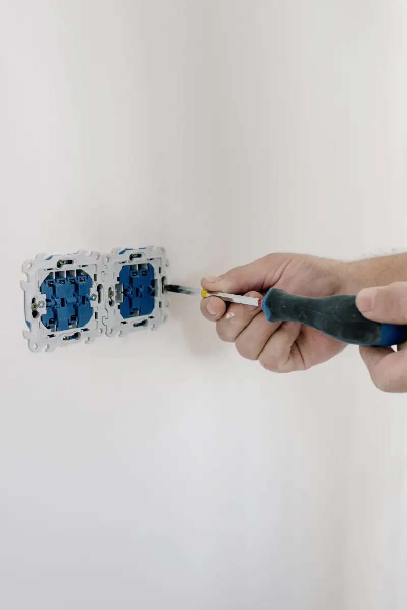 Manos con destornillador instalando un mecanismo eléctrico en una pared de casa
