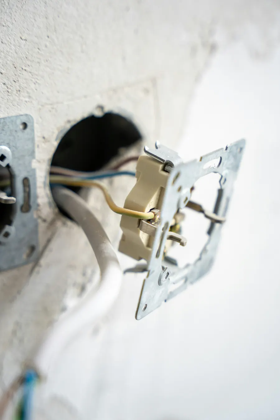 Toma eléctrica abierta con el cableado a la vista en una pared