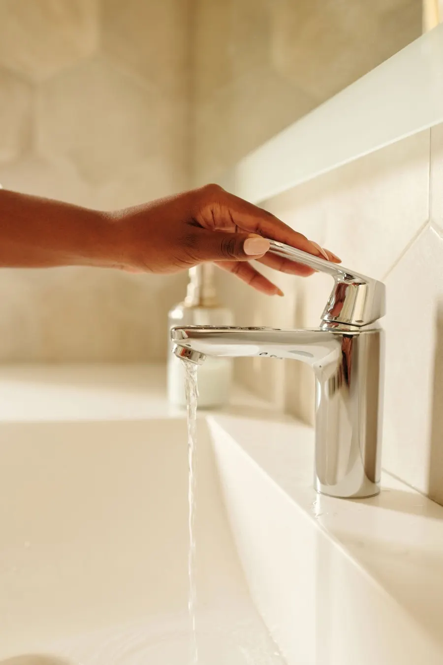 Hand turning on a bathroom tap with water flowing