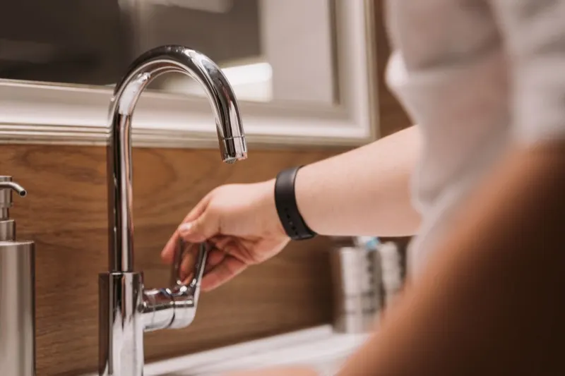 Hand turning a tap over a clean kitchen sink